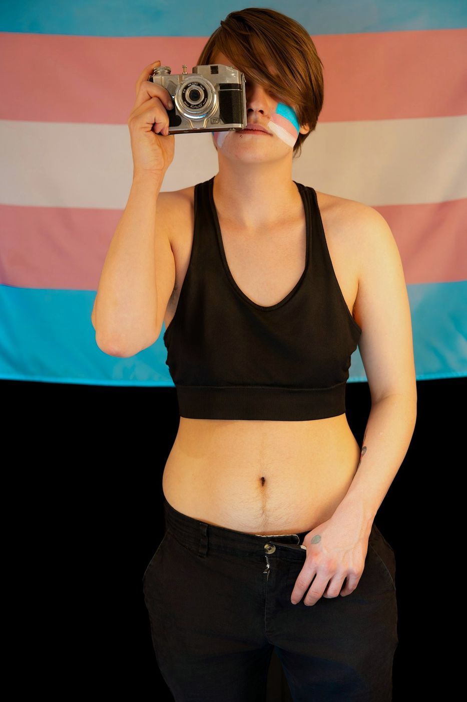 A creator holding a camera in front of a trans pride flag