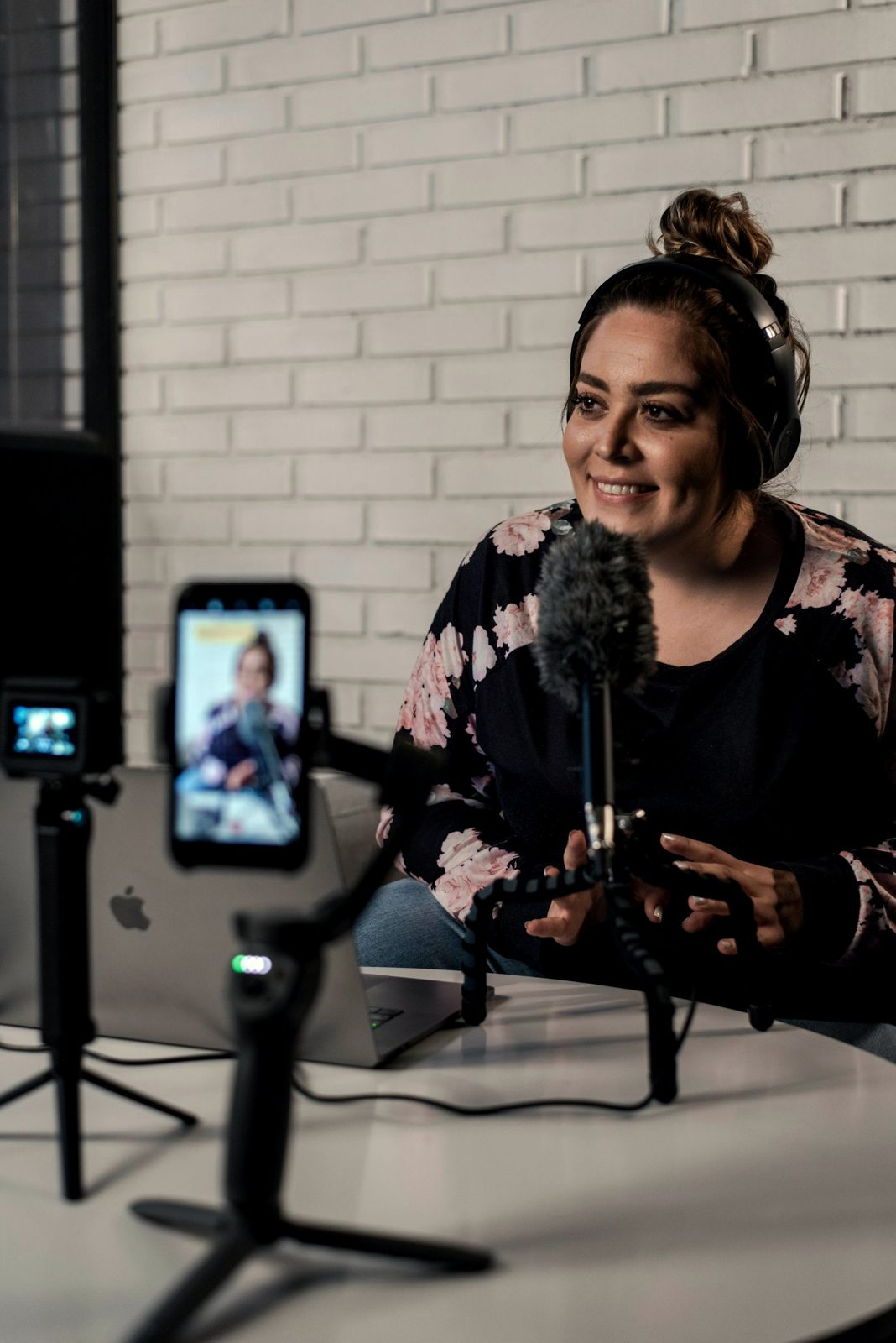 A creator smiles as she films herself on a phone rig at her desk, mic in front of her