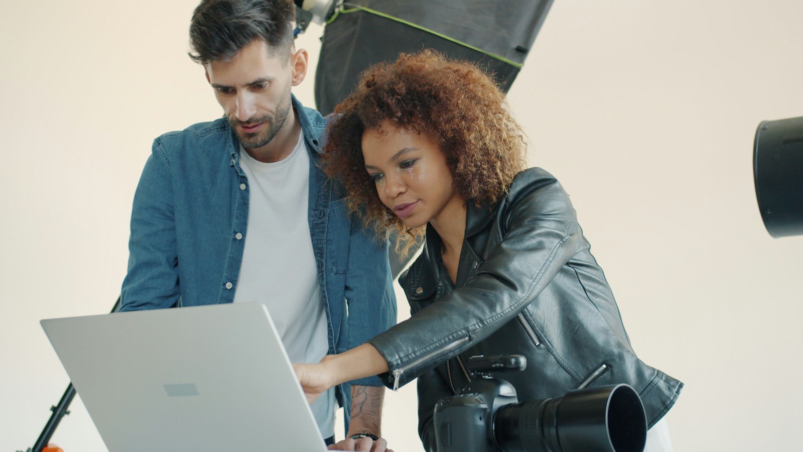 Two creators in a photo studio leaning over a laptop together, calmly looking at the screen