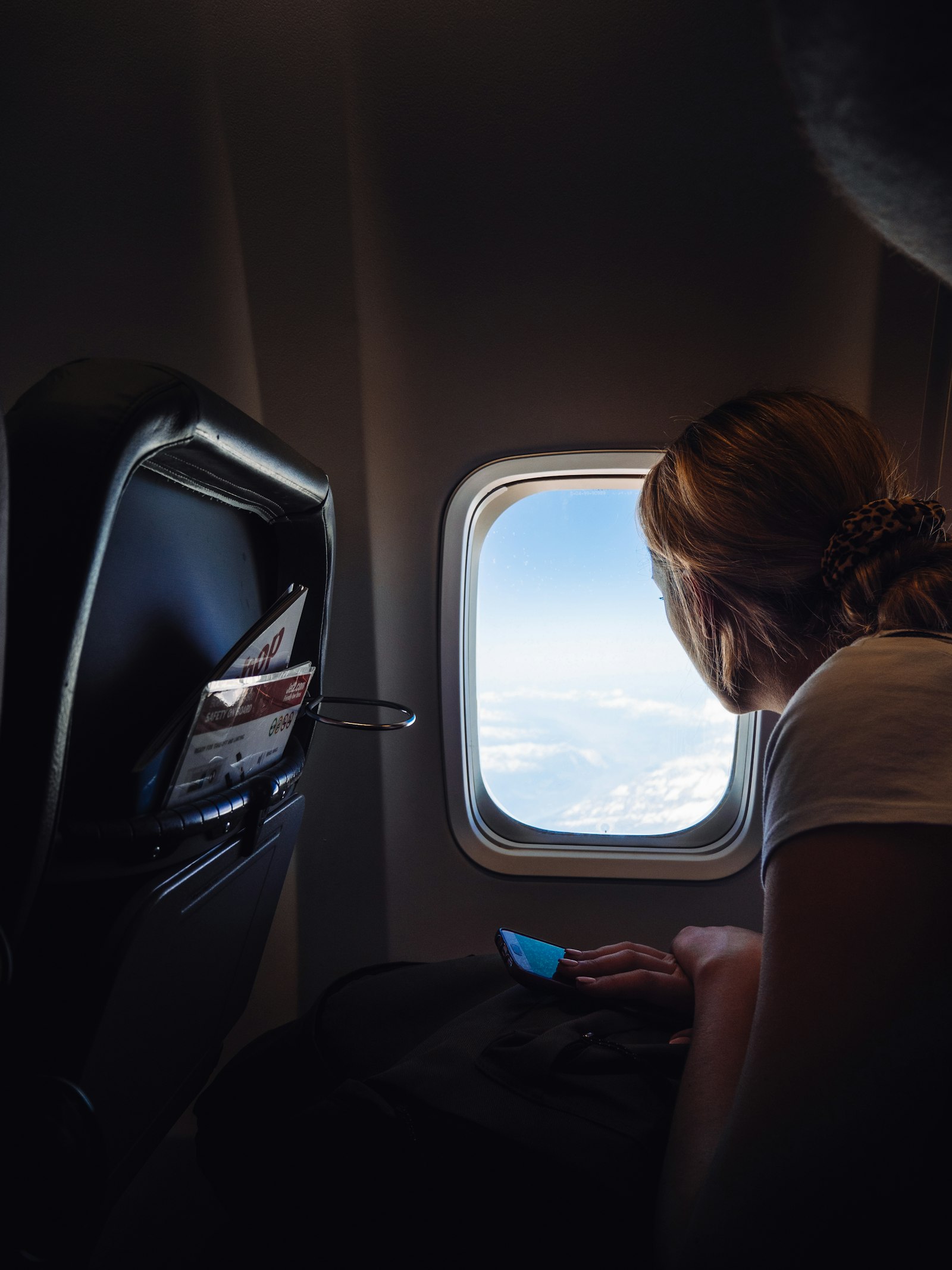 A woman in a plane seat looking out the window at the clouds